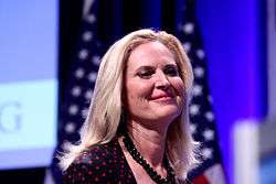 Photograph of Ann Romney taken in a hall, with large video screen and 